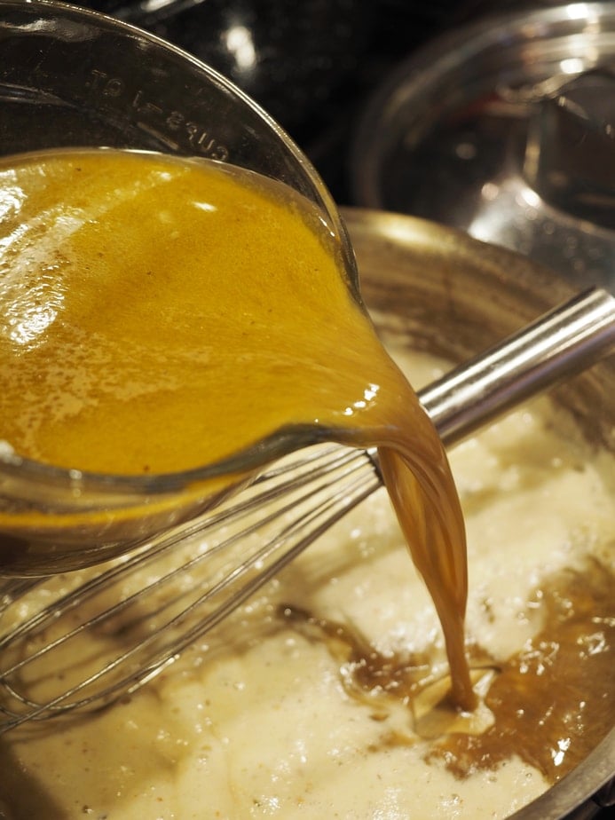 Pouring giblet turkey stock into roux, whisking until thick for how to make gravy from scratch.