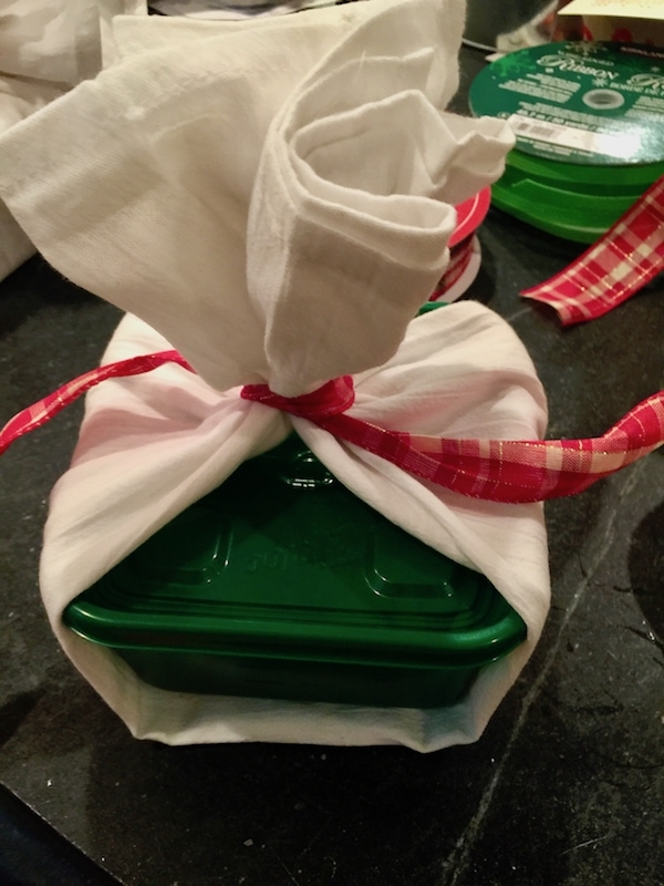 Wrapping up seasonal ziplock container with flour sack towel and festive ribbon, containing cookie dough balls. 