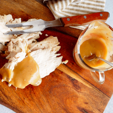 Easy turkey giblet gravy square image with sliced turkey breast on cutting board poured with rich turkey gravy.