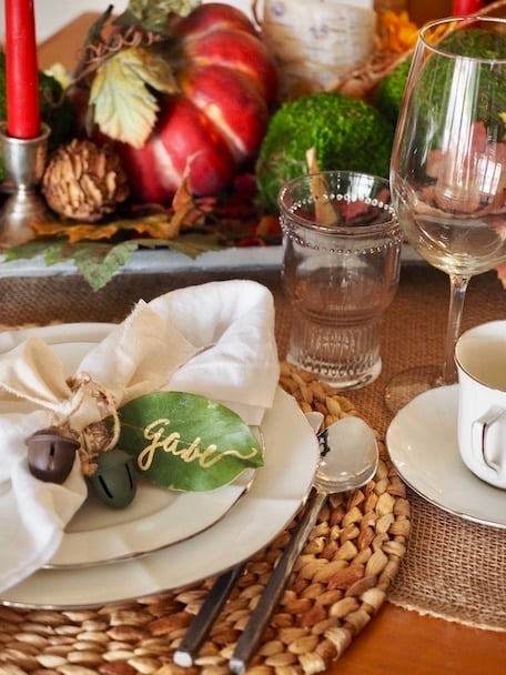 A rustic Thanksgiving tablescape using fresh bay leaves as name cards, rattan chargers.
