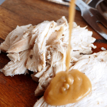 Turkey giblet gravy square image with turkey breast sliced on cutting board and pouring rich turkey giblet gravy over the top.