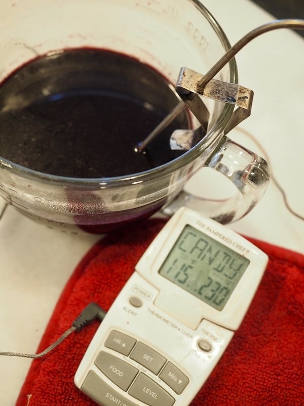 food thermometer (digital) with 115 degrees show and probe inside mixing bowl with elderberry syrup.