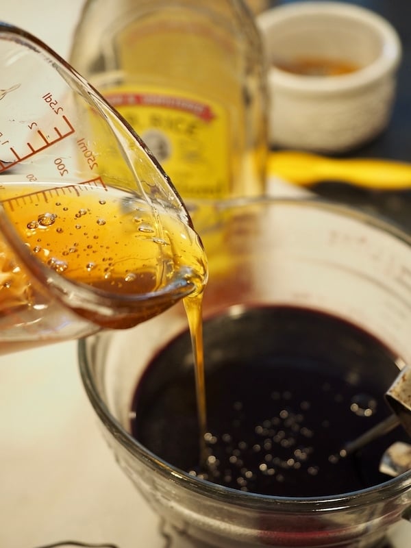 pouring honey into finished and cooled elderberry syrup in large mixing bowl. 