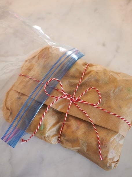 Sliding a piece of parchment packaged cookie dough balls into a ziplock baggie.