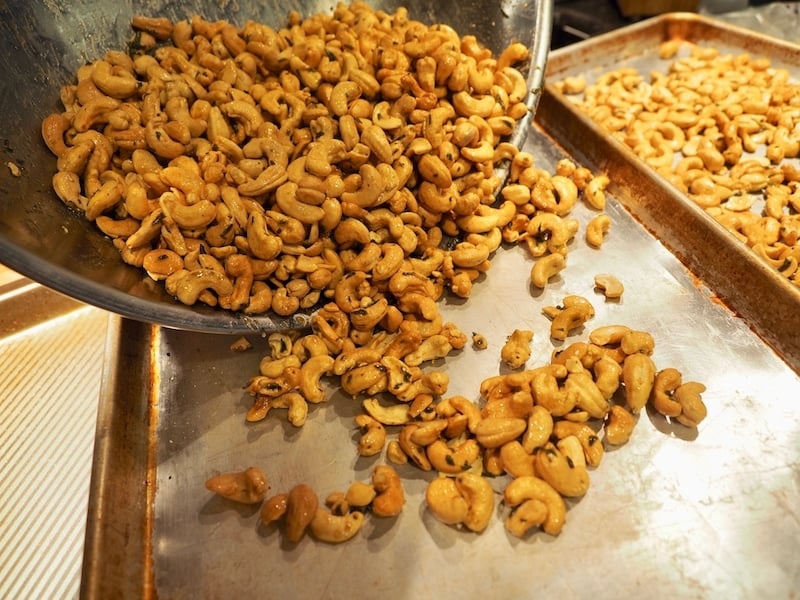 pouring baked cashews onto sheet pan for baking. 