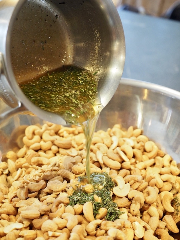 pouring butter, rosemary mixture onto cashews. 