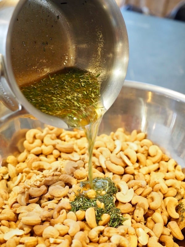 pouring butter, rosemary mixture onto cashews.