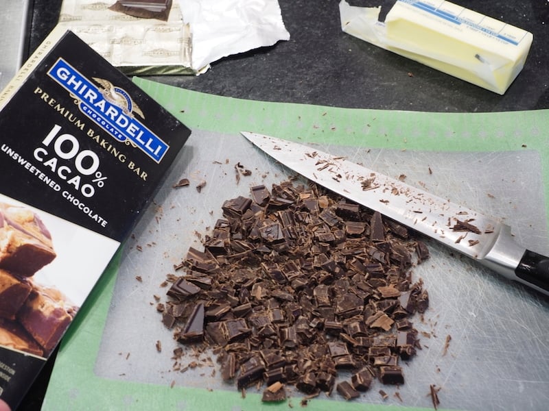 Chopped Ghirardelli 100% cacao unsweetened chocolate bar and chopped chocolate on cutting board with knife. 