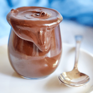 Old fashioned hot fudge sauce in a pretty glass jar with a silver spoon.