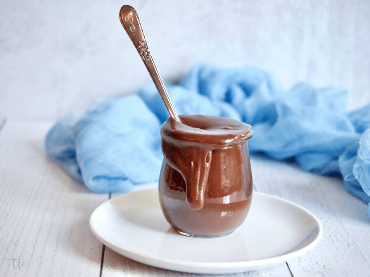 Old fashioned hot fudge sauce in pretty tulip jar with a spoon in the jar.