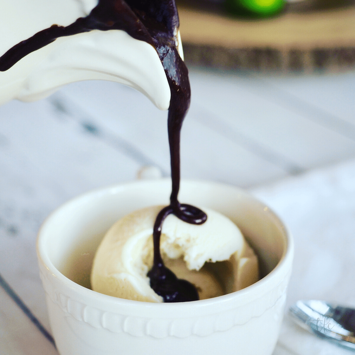Square image of pitcher pouring old fashioned hot fudge sauce onto vanilla ice cream.