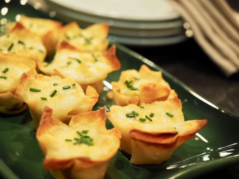 Finished artichoke cheese wontons on green ceramic tray with chopped chives sprinkled on top. Artichoke Cheese Wontons | www.thefreshcooky.com