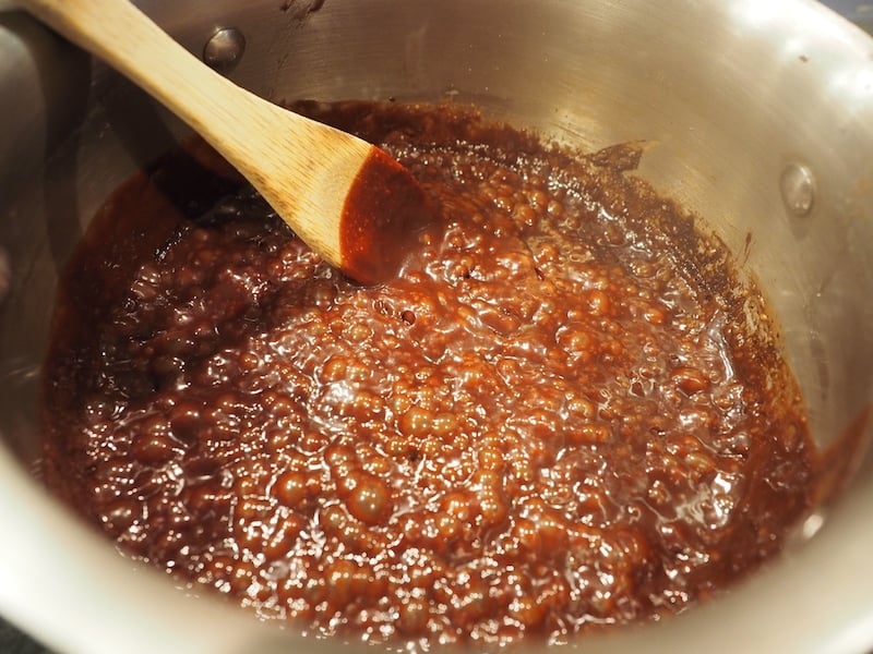 Hot fudge mixture at a simmer with wooden spoon in sauce pan.