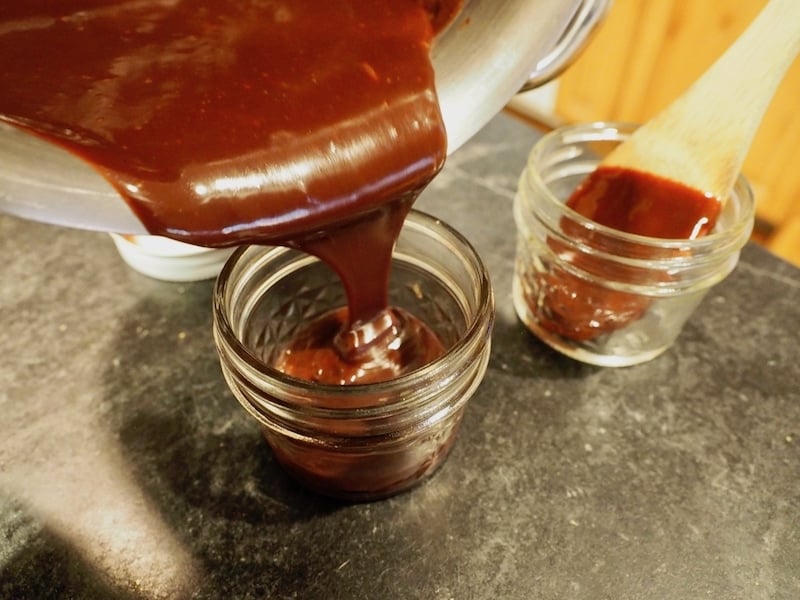 Pouring old fashioned hot fudge sauce into small mason jars for gifting and storage.