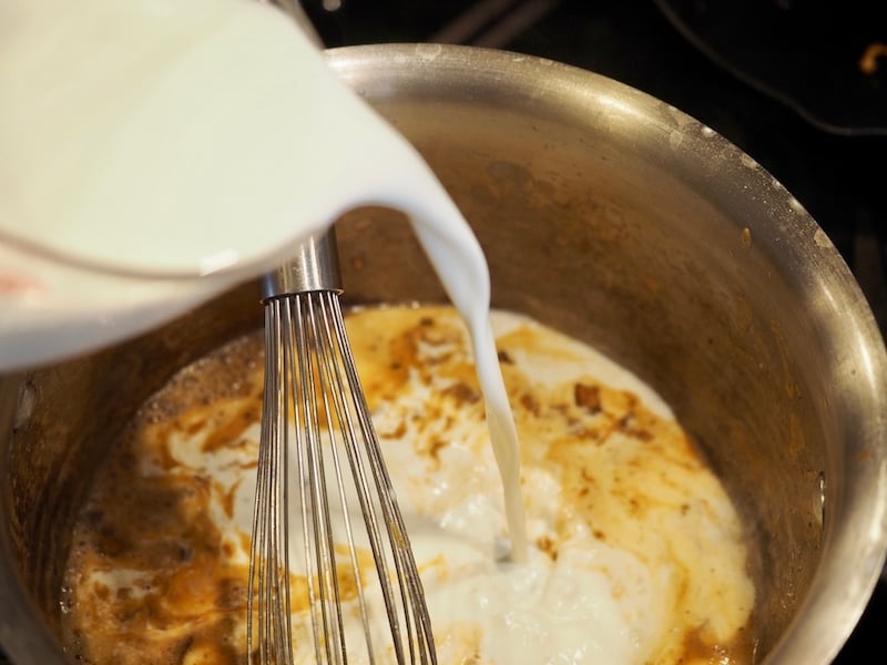 pouring in half and half into roux mixture with whisk sitting in a medium pot.