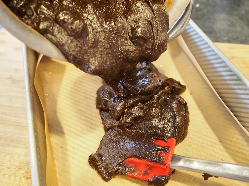 pouring brownie batter into parchment lined 9x13 inch pan with red spatula. 