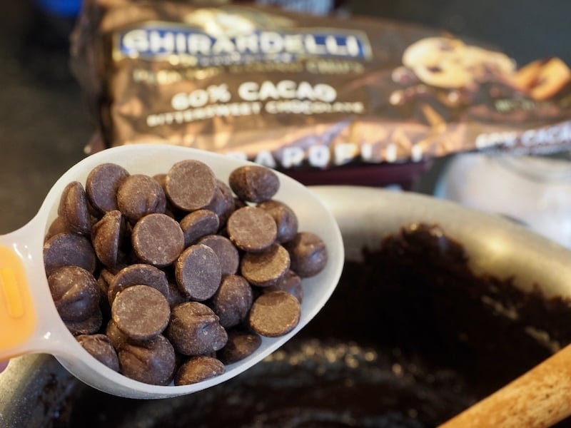 measuring cup with chocolate chips over pot of brownie mixture, ghirardelli chocolate chip bag in background.