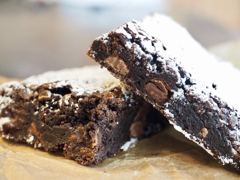 two soft and gooey brownies, dusted with powdered sugar on parchment paper
