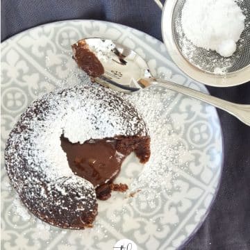 lava cake on gray patterned plate open with oozing "lava" dusted with powdered sugar with blue napkin below.