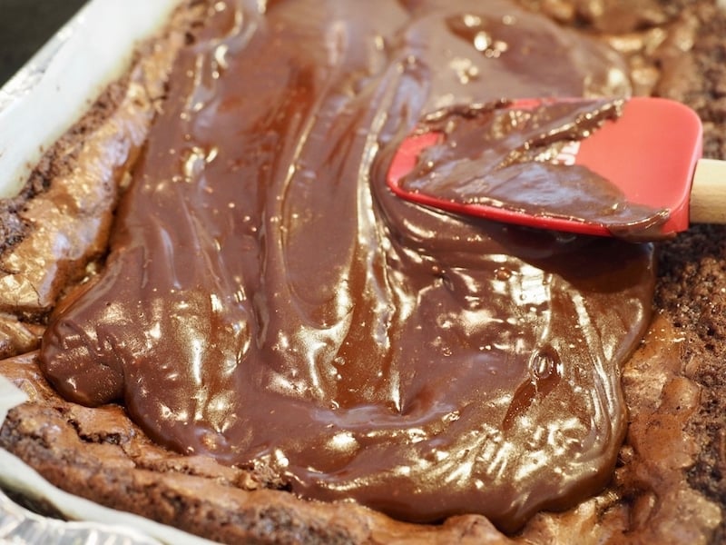 Spreading frosting with red spatula on top of warm brownies.