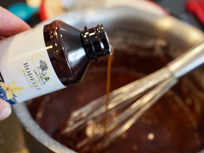 pouring Rodelle vanilla extract into frosting mixture in pot with whisk