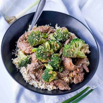Easy Beef and Broccoli image in black bowl with green onions on tea towel underneath, spoon in bowl.