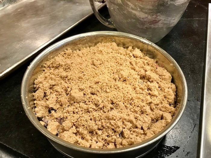 Blueberry Crumb Cake in spring form pan ready to go into oven with mixing bowl and sheet pan in background. 