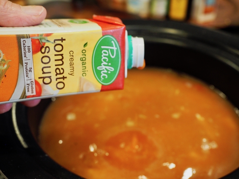 holding a small carton of organic creamy tomato soup from Pacific brand.