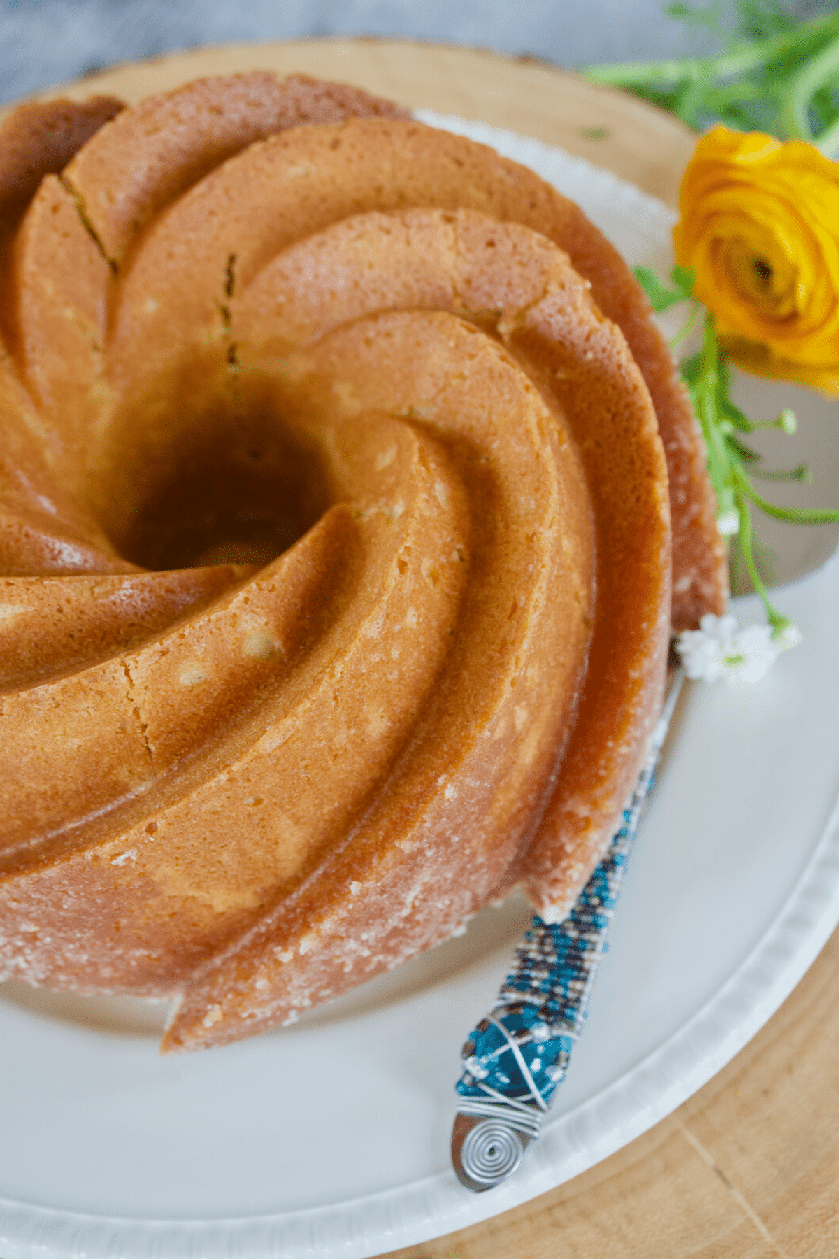 Image of old fashioned butter pound cake on platter with server and a pretty flower.