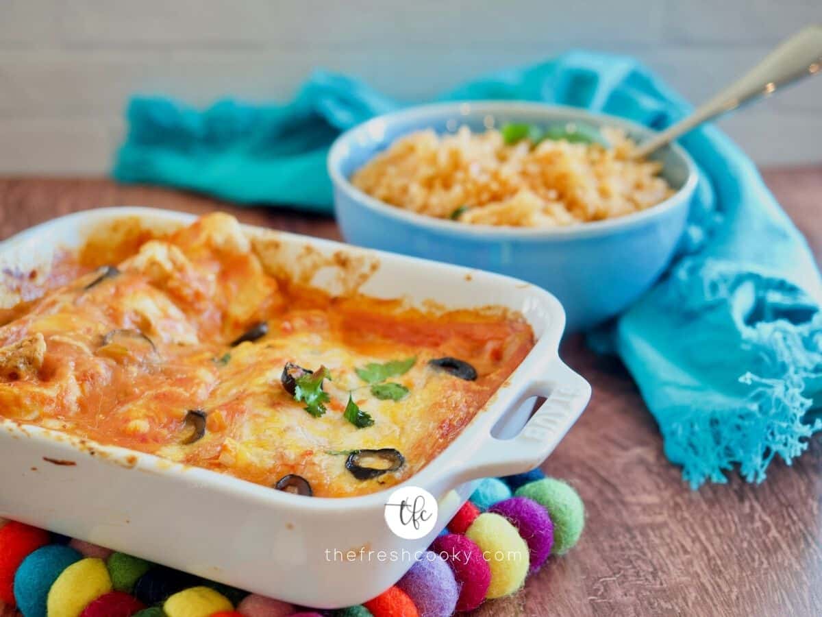 FB image with casserole dish filled with cheesy enchiladas and bowl of spanish rice in background.