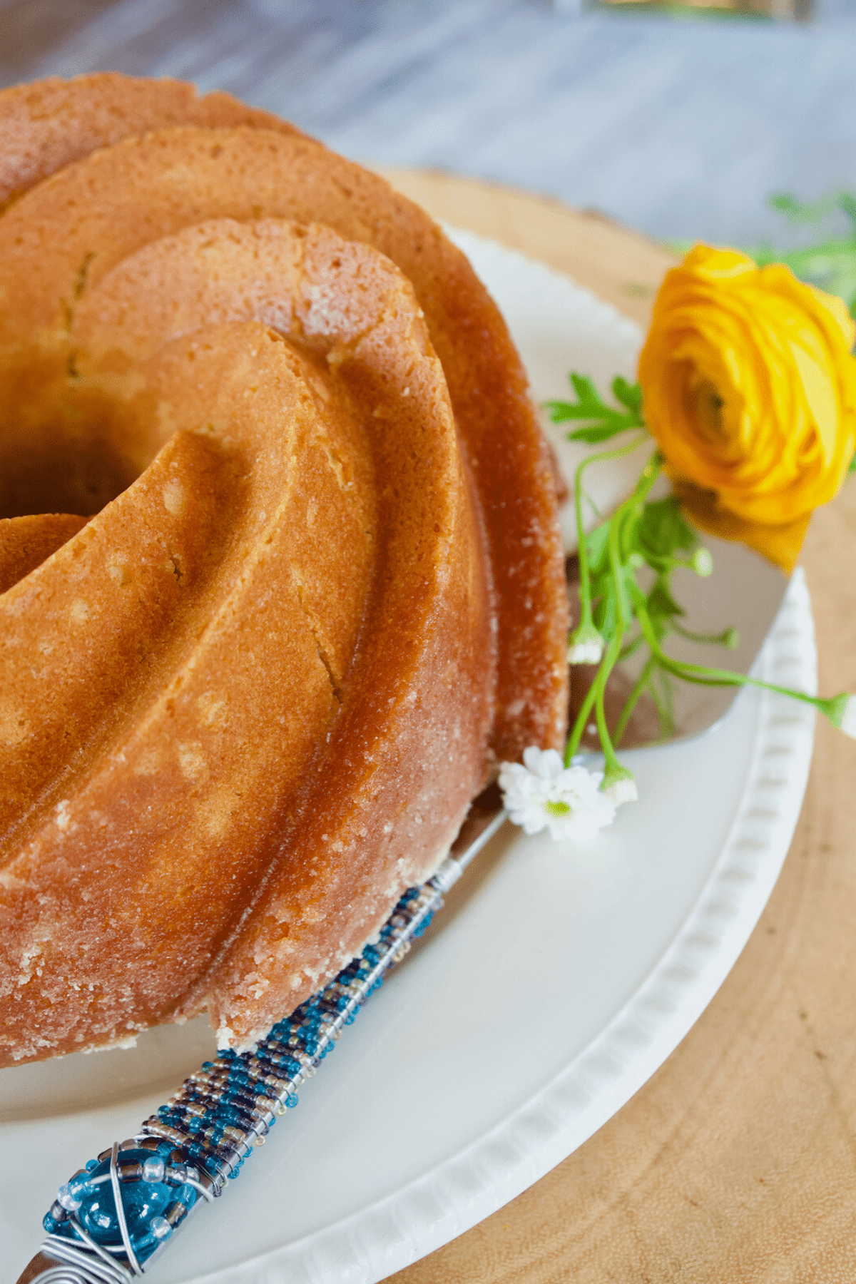 Old fashioned butter pound cake on platter with flower and serving utensil.