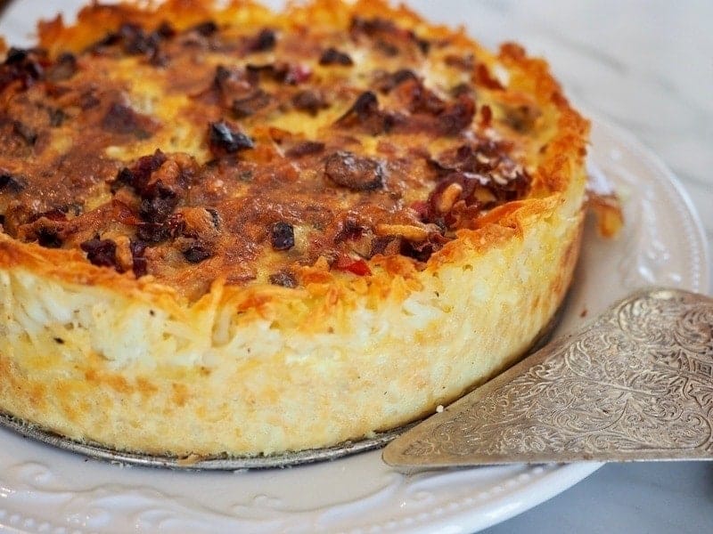 Image of prosciutto and gruyere quiche on white platte, with silver pie server near front of plate. 