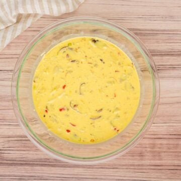 Egg mixture with veggies mixed in in glass bowl.