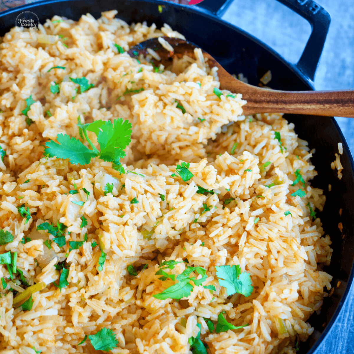 Vegetarian spanish rice in large cast iron skillet with wooden spoon.