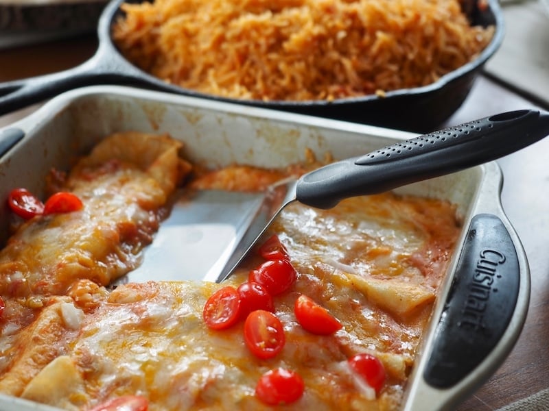 Melty cheese enchiladas in a baking pan with large spatula grabbing one of the enchiladas.