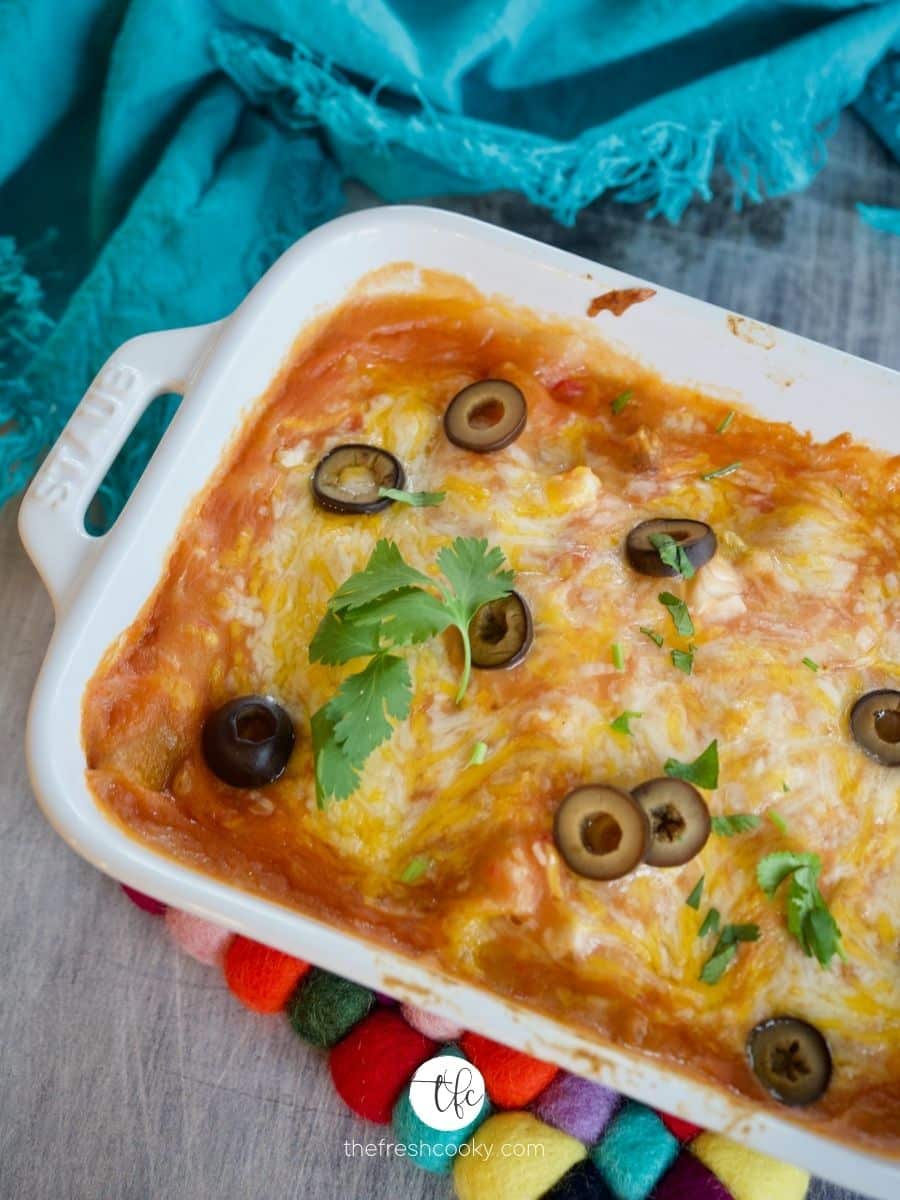 top down shot of cheese enchiladas with brightly colored hot pad beneath, sprinkled with sliced black olives.