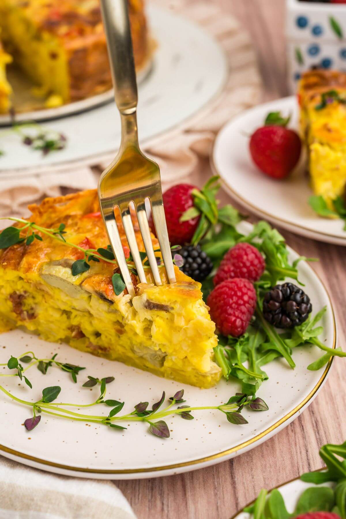 Fork in a slice of prosciutto quiche on a plate with a fresh salad and herbs.