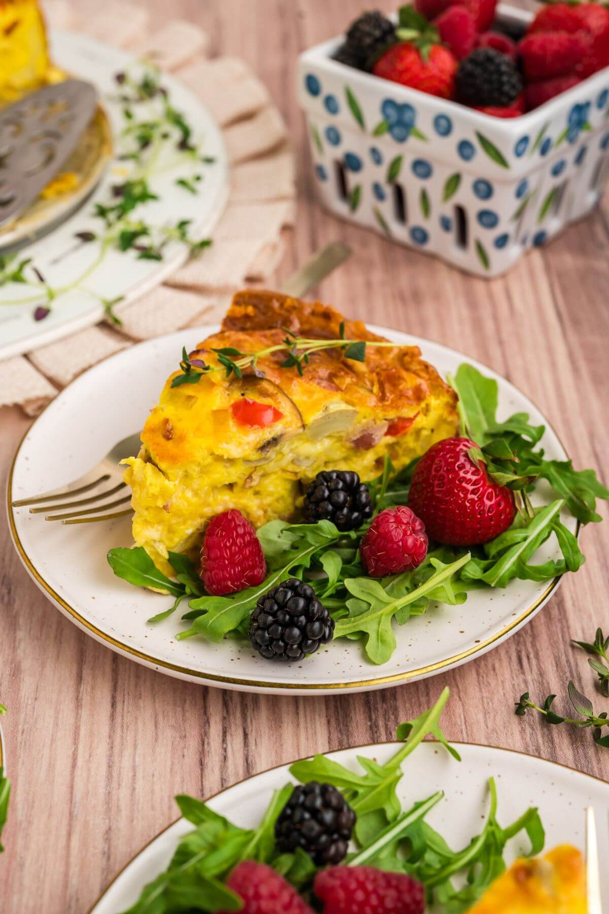 Slice of hash brown crust quiche on a plate with a berry and green salad.