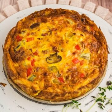 Hash brown crust quiche on tray with fresh herbs.