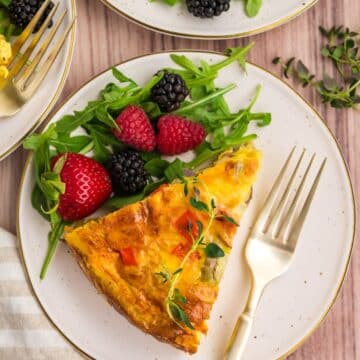 A wedge of hash brown quiche on a plate with a arugula. and berry salad.