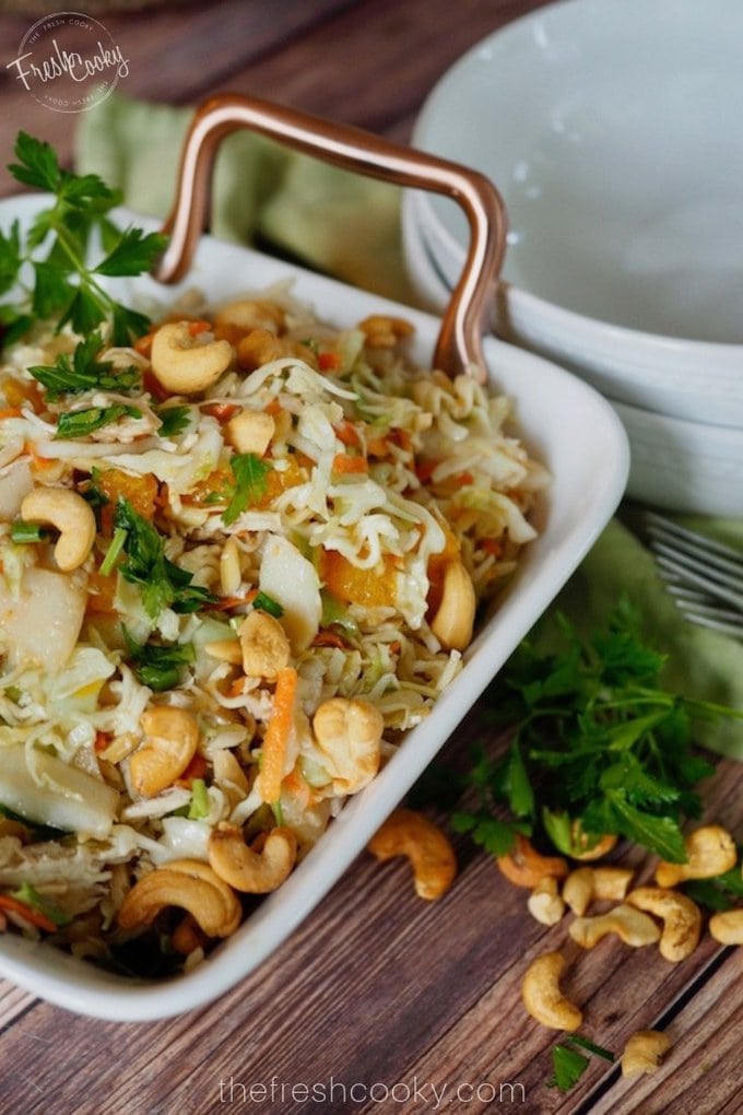 A pinterest image for Asian Ramen Noodle Salad with a square bowl with a cabbage salad, mixed with ramen noodles, cashews, cilantro, mandarin oranges with asian dressing 