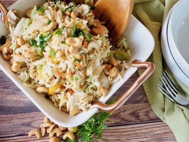 Photo of an asian ramen noodle salad with mandarin oranges, cashews, ramen noodles, parsley and coleslaw in a bowl ready to be served.  