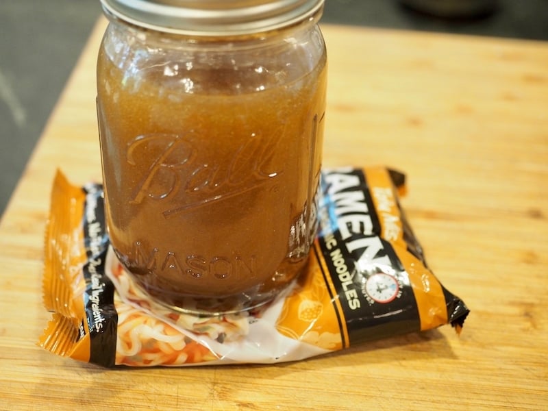 Mason jar full of dressing, crushing a bag of ramen noodles for salad.