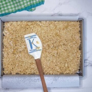 Pressing rice krispie treats into a prepared 9x13 inch pan, lined with parchment.