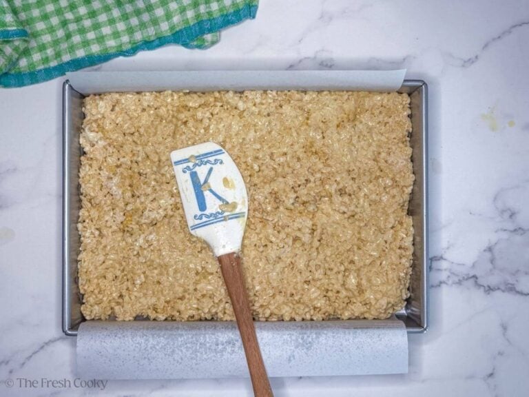 Pressing rice krispie treats into a prepared 9x13 inch pan, lined with parchment.