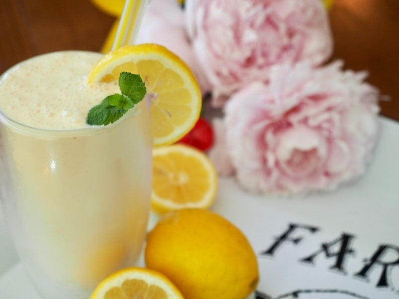 Frozen lemonade in a glass with a straw, lemons and flowers in background | www.thefreshcooky.com 