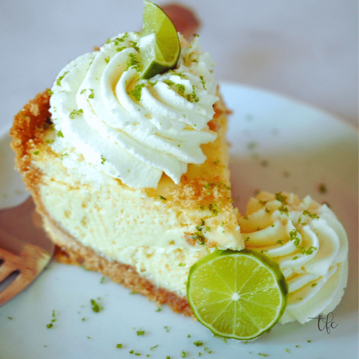 Slice of key lime pie topped with dollops of whipped cream and sliced limes. 