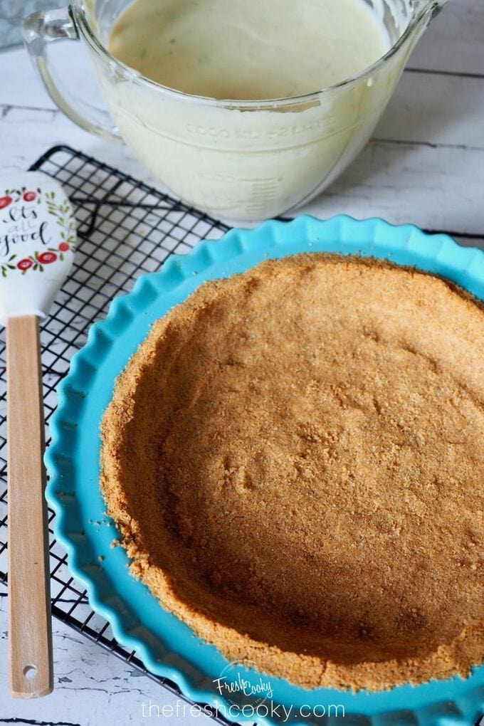 Image of empty graham cracker crust with spatula, near a mixing bowl filled with best key lime filling.