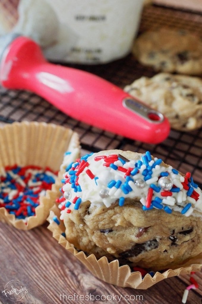 Pin for chocolate chip cookie ice cream sandwiches with red white and blue sprinkles, in a parchment cupcake liner with an ice cream scoop, cookies and ice cream behind. Recipe on the freshcooky.com