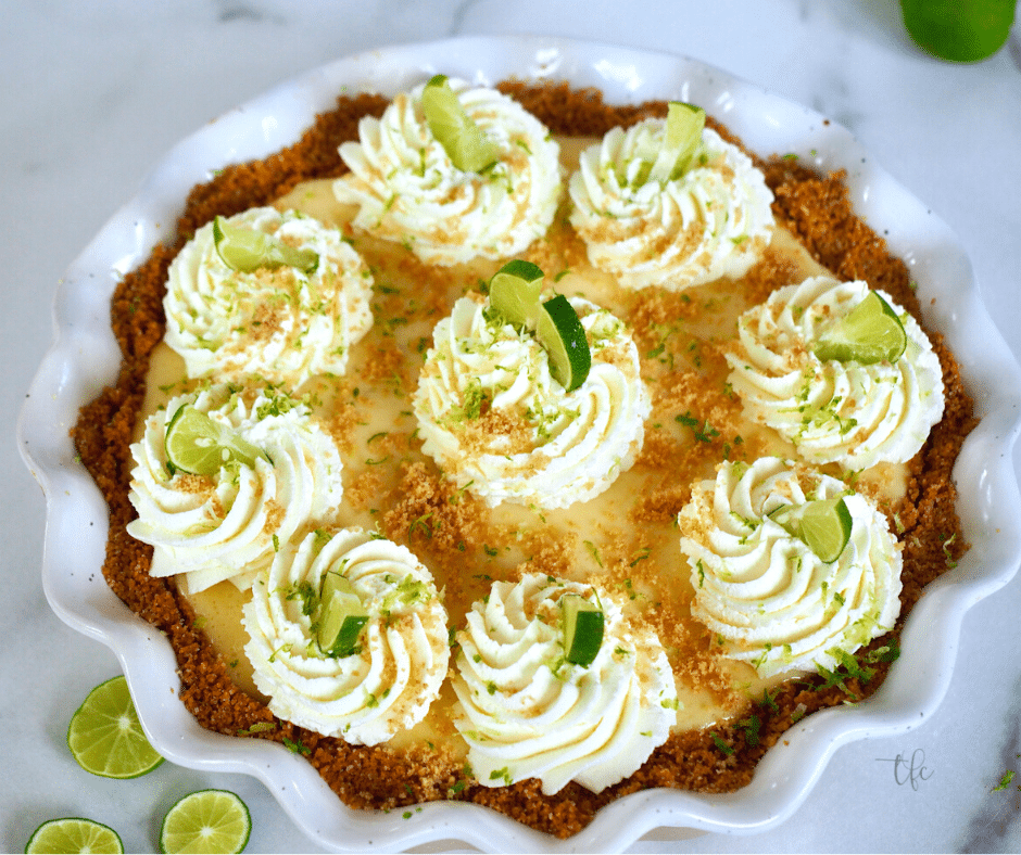 Easy Key Lime Pie image of top down shot of decorated key lime pie with swirls of whipped cream and decorated with wedges of lime.